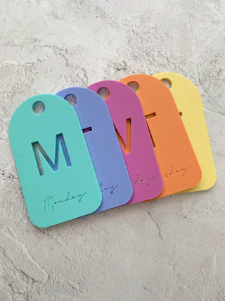 Five colourful tags with 'M' and 'Monday' text on a textured gray surface