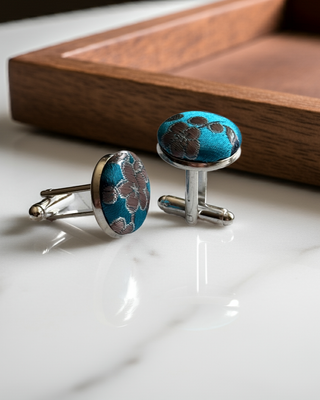 Pair of blue floral patterned cufflinks on a white surface with a wooden tray in the background.