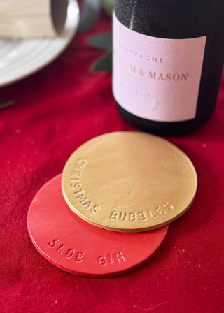 Two gold and red coasters with text on a red surface next to a bottle of M & Mason champagne.