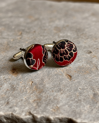 Red and black floral patterned cufflinks on a stone surface