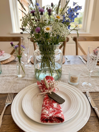 Dining table setting with a vase of wildflowers, plates, and cutlery. Olive Leather napkin ring stamped with James