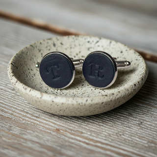 Pair of Leather cufflinks with 'R' initials on a speckled ceramic dish.