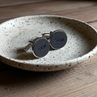 Cufflinks with 'S&W' stamped on navy leather, on a speckled ceramic dish on a wooden surface