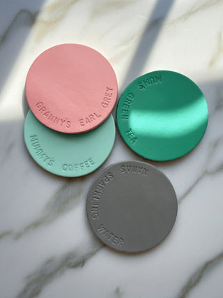 Four round coasters in pink, green, and gray on a marble surface
