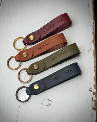 Four leather keychains with engraved text on a wooden surface