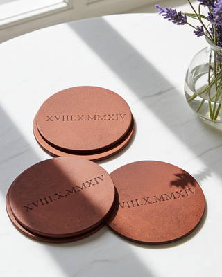 Round leather coasters with personalized embossed text on a marble surface with a vase of lavender.