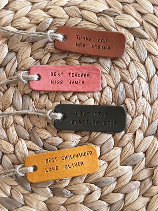 Five leather tags with personalised messages on a woven surface. Gifts tags for teachers made out of leather complete with rustic twine.