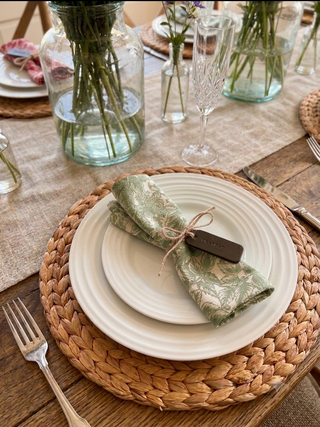 Table setting with white plates, green napkins, and a woven placemat. Green leather label stamped with Grandad.