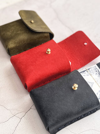 Three leather card holders in green, red, and black on a light grey surface.