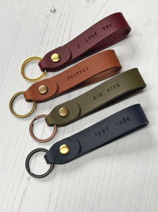Four leather keychains with engraved text on a light wooden surface