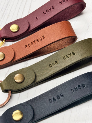 Four leather keychains with stamped text on a white background