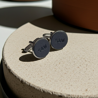 Pair of navy blue cufflinks with 'S&W' engraving on a textured beige surface.
