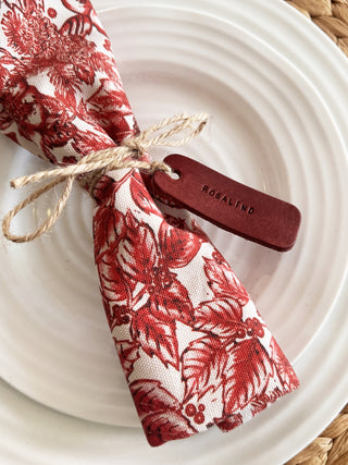 Red and white patterned napkin with a red leather tag stamped with 'Rosalind' on a white plate