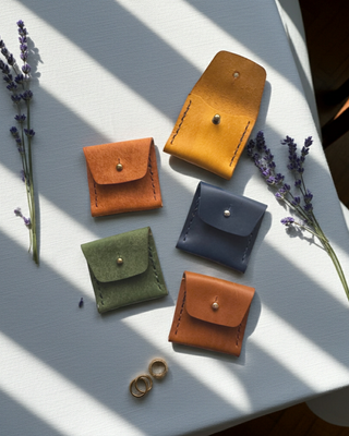 Five small leather pouches in different colors on a white surface with lavender flowers.