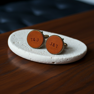Tan Round leather cufflinks with 'T&J' engraving on a white stone surface.