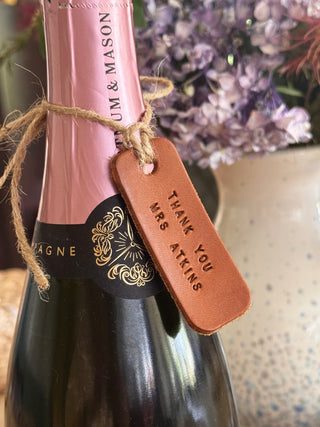 Pink champagne bottle with a tan leather hand stamped tag and floral background. Gift for teacher