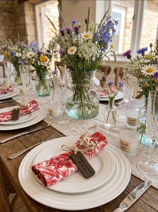 Dining table set with floral centerpieces, plates, and cutlery in a rustic setting. Leather Tag stamped with wedding date and names of the bride and groom.