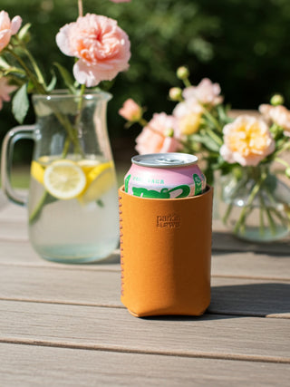 Can in a yellow sleeve on a wooden table with flowers and a pitcher in the background