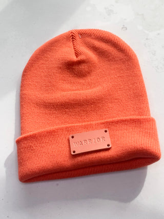 Salmon pink leather tag with the word WARRIOR on a coral hat.